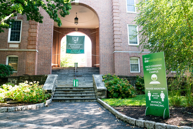 Photograph of entrance to Manhattan College campus Quad with signage about social distancing (six feet) while on campus.
